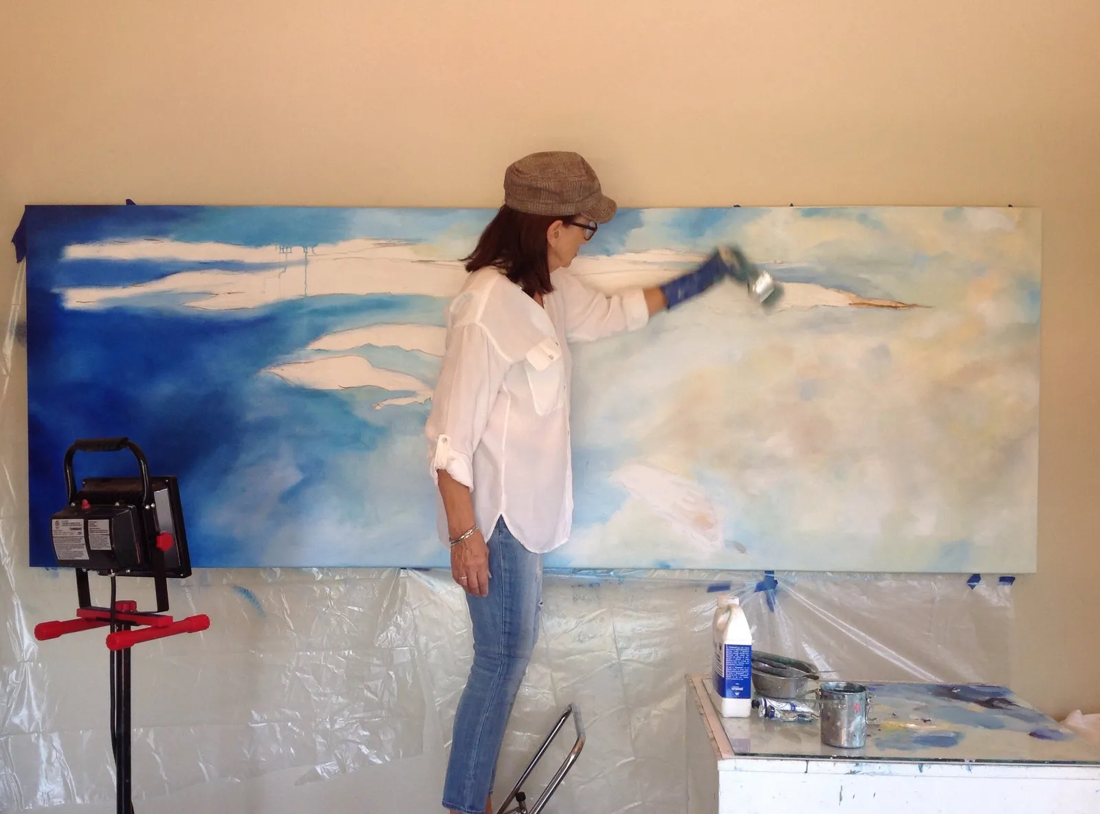 Michele Zuzalek in her studio, painting a large canvas of blue sky and clouds