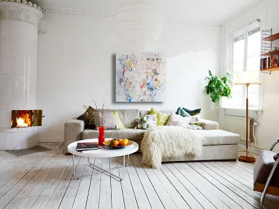 A colorful abstract painting above a sofa in a bright white living room with a fireplace