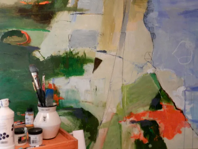 Close-up of a colorful abstract work in progress, with brushes and paint jars in front of it